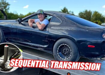 A man leans out of the window of a dark Toyota Supra sports car on a trailer; inset shows a Sequential Gearbox shifter. Text reads "SEQUENTIAL TRANSMISSION.