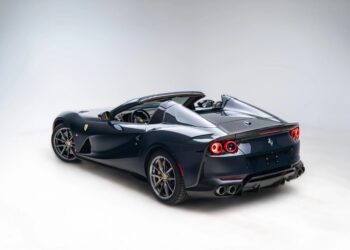 A dark blue Ferrari convertible sports car is shown in a studio with its roof down, viewed from the rear three-quarter angle.