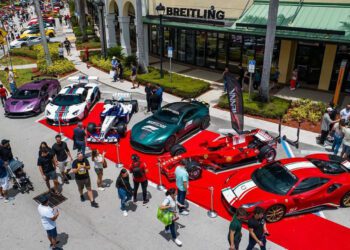 Several sports cars, including a striking Praga Bohema hypercar, are displayed on a red carpet outside a Breitling store as crowds explore this highlight of the South Florida automotive weekend.