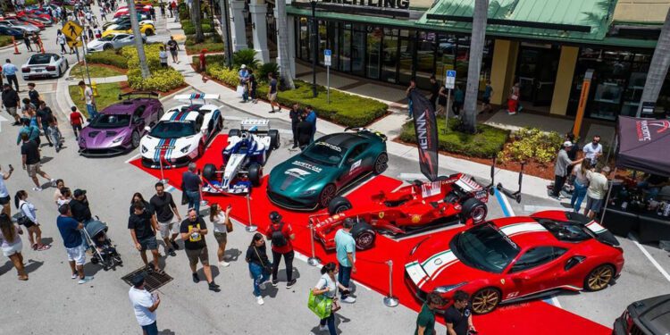 Several sports cars, including a striking Praga Bohema hypercar, are displayed on a red carpet outside a Breitling store as crowds explore this highlight of the South Florida automotive weekend.