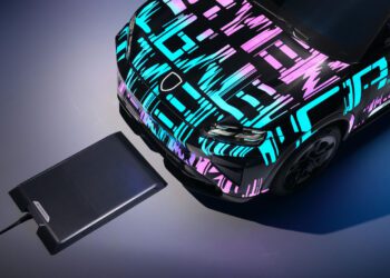 A Porsche Cayenne Electric with a colorful geometric wrap is positioned above a wireless charging pad, demonstrating how it works as an advanced electric vehicle charging system.