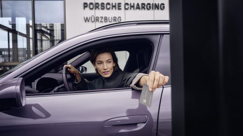 A person in a purple New Porsche holds a card toward a charging station at a Porsche Charging location in Würzburg.
