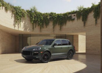 A green Porsche Sonderwunsch SUV is parked in the center of a circular open courtyard with beige stone walls and greenery above.