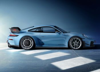 A blue sports car is parked on a concrete surface under bright lighting, shown from the side against a gradient blue background.