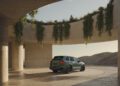A green Transformed Cayenne GTS is parked under a circular concrete structure with pillars and hanging plants, with sand dunes visible in the background.