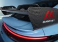 Close-up of a blue Porsche GT3’s rear end, featuring a large carbon fiber rear wing with red “Manthey” branding and prominent aerodynamic elements.