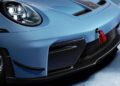 Close-up of the front end of a blue Porsche sports car, showing the headlight, red tow strap, grille, carbon fiber details, and part of the wheel.