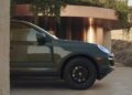 A dark green Transformed Cayenne SUV parked on a stone driveway next to a modern building with copper walls and greenery.