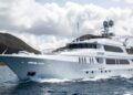 A large white luxury yacht cruises on blue ocean water with green hills and a cloudy sky in the background, offering a true maritime experience.
