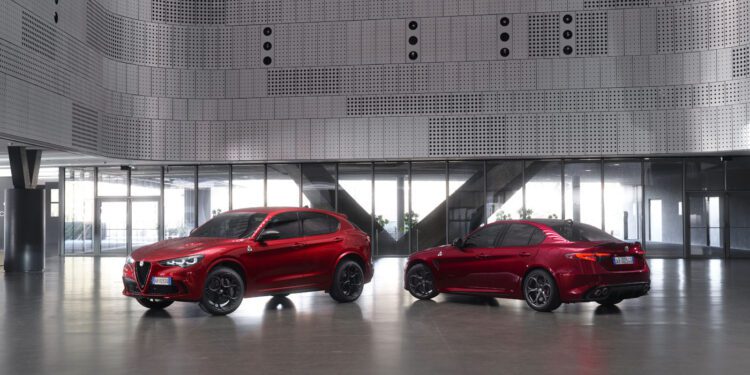 Two red Alfa Romeo vehicles, an SUV and a sedan, are parked inside a modern building with metallic perforated walls and large windows.