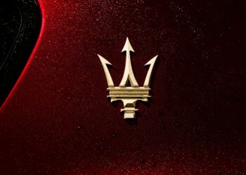 Gold Maserati trident logo on a red, water-speckled car surface.