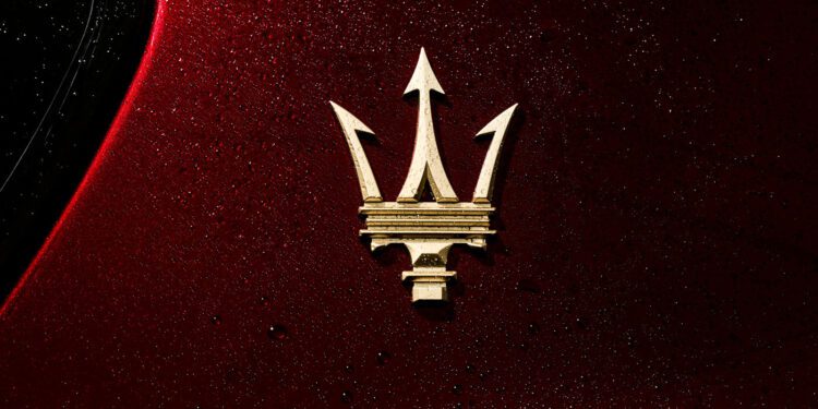Gold Maserati trident logo on a red, water-speckled car surface.