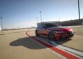 A red Alfa Romeo sedan driving on an empty racetrack under a clear blue sky.