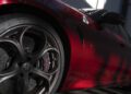 Close-up of a red Alfa Romeo Giulia Quadrifoglio, focusing on the front alloy wheel and brake disc, with shadows and light patterns playing across the vehicle’s body.