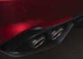 Close-up of an Alfa Romeo’s rear bumper, showcasing two Akrapovič-branded exhaust pipes and a red reflector above them—typical design cues of the high-performance Stelvio Quadrifoglio.