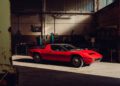 A red classic Maserati sports car is parked inside an old, dimly lit garage with industrial equipment and workbenches in the background, capturing the spirit of Maserati’s 111th Anniversary.