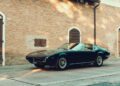A classic black Maserati sports car is parked on the street in front of a brick building with arched doors and windows, celebrating Maserati’s 111th Anniversary in timeless style.