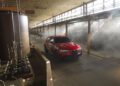 A red Alfa Romeo Stelvio Quadrifoglio SUV is parked inside a large industrial warehouse, with sunlight filtering through upper windows and visible machinery on the left.