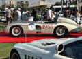A classic silver race car with "1955" on the side is displayed on a red carpet at an outdoor car show during the 1000 Miglia Experience UAE 2025: Opening Day Highlights, with people and other cars in the background.