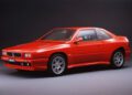 A red two-door Maserati Shamal coupe is parked in a studio setting against a dark background, celebrating the brand’s 111th Anniversary.