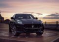 A black Maserati SUV is parked on a tiled surface near a waterfront at sunset, with buildings and railings in the background—perfectly capturing the elegance of the Maserati 111th Anniversary.