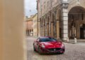 A red Maserati anniversary edition sports car is parked on a cobblestone street lined with historic buildings and arches.