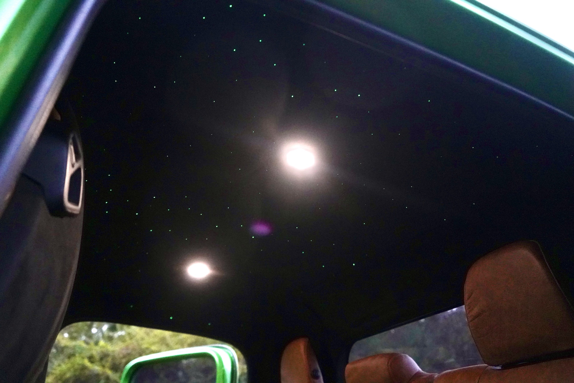 Interior view of a Dodge Power Wagon Crew Cab for sale, featuring brown seats, a black ceiling with LED star lights, two overhead lights, and part of a green door.