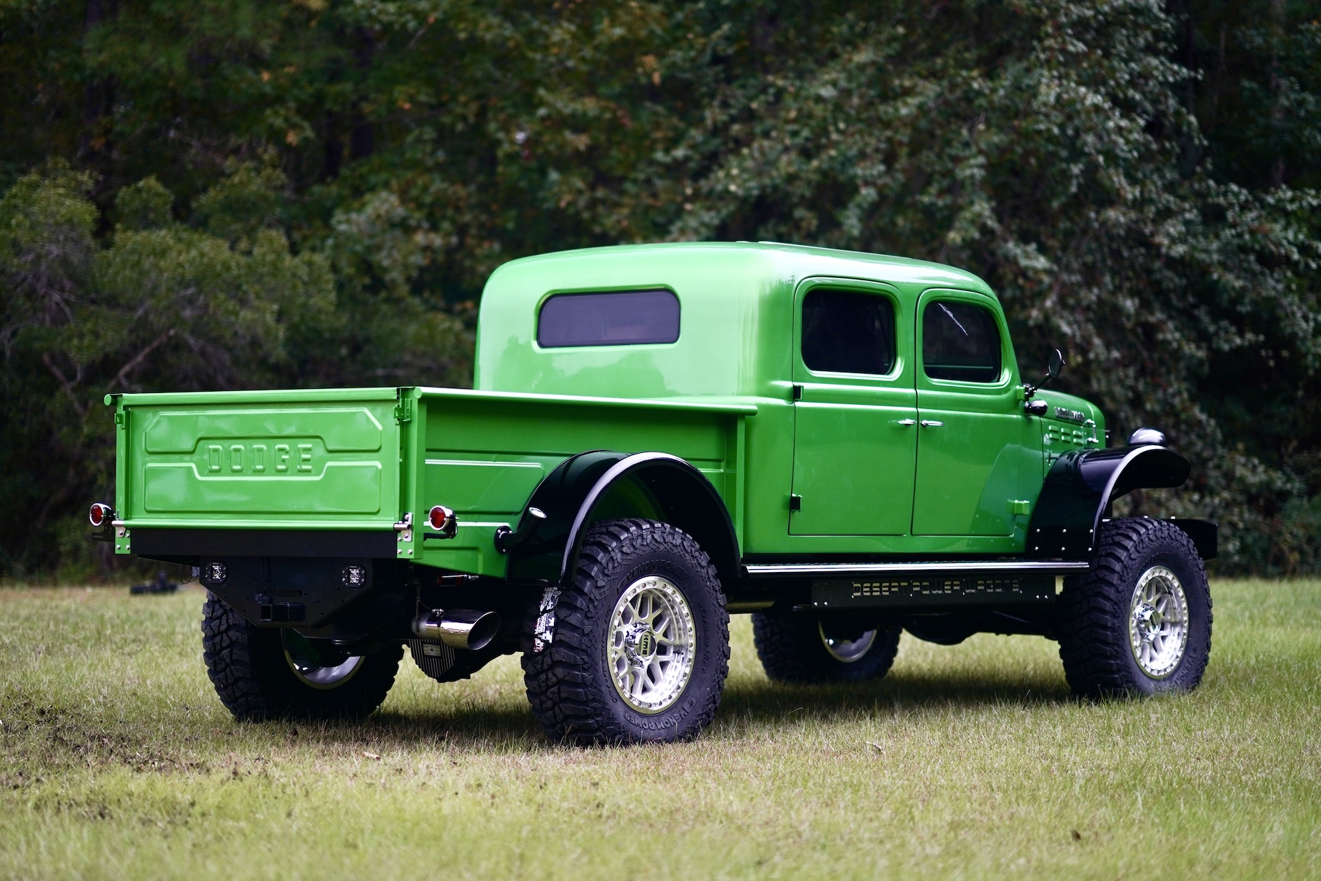 A bright green vintage Dodge Power Wagon pickup with large off-road tires and crew cab is parked on grass near trees—now for sale.