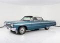 A blue 1964 Chevrolet Impala convertible with a white soft top is parked in a white studio setting, capturing the timeless appeal of classic muscle cars.