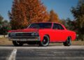 A red classic muscle car is parked on asphalt in front of autumn trees under a clear blue sky, capturing the timeless appeal of Classic Muscle Cars.