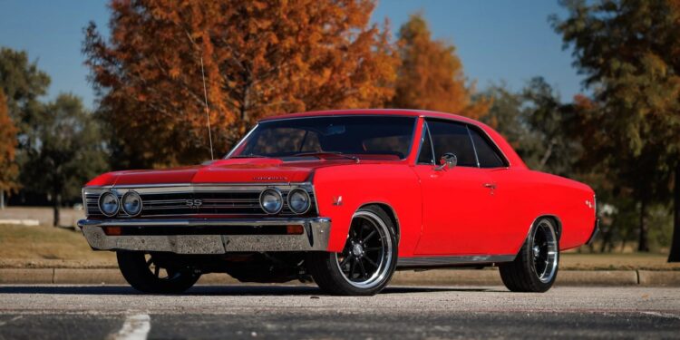 A red classic muscle car is parked on asphalt in front of autumn trees under a clear blue sky, capturing the timeless appeal of Classic Muscle Cars.