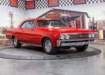 A high-performance red 1967 Chevrolet Chevelle SS coupe is displayed indoors on a rotating platform, with a vintage-themed backdrop featuring Western and Coca-Cola imagery.