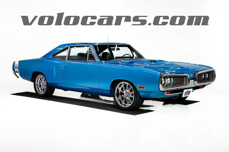 A bright blue classic muscle car with chrome rims is displayed in a studio setting; "volocars.com" is written above the car, showcasing one of the finest classic muscle cars for sale.