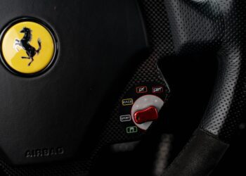 Close-up of a Ferrari steering wheel showing the logo, airbag label, and drive mode selector—offering a glimpse of Your Chance To Own The Final Ferrari That Michael Schumacher Helped Develop.