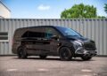 A black luxury van with tinted windows and black alloy wheels is parked on pavement in front of a gray shipping container, showcasing the premium appeal of FariCars' luxury vans.
