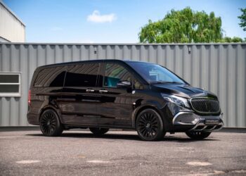 A black luxury van with tinted windows and black alloy wheels is parked on pavement in front of a gray shipping container, showcasing the premium appeal of FariCars' luxury vans.