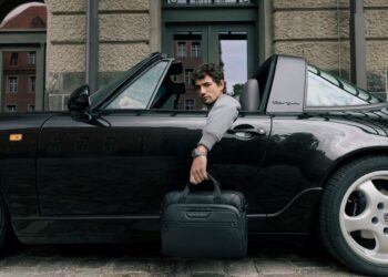 A man sits in a black Porsche Design convertible sports car with the door open, holding a black briefcase, parked in front of a building—a scene worthy of any 2025 Holiday Gift Guide.