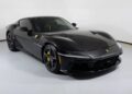 A black Ferrari 12Cilindri sports car with yellow brake calipers is displayed in a well-lit showroom with a white background, highlighting this exceptional 2025 Ferrari for sale.