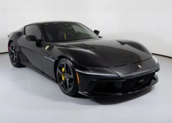 A black Ferrari 12Cilindri sports car with yellow brake calipers is displayed in a well-lit showroom with a white background, highlighting this exceptional 2025 Ferrari for sale.
