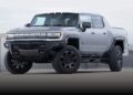 A silver GMC Hummer EV pickup truck, featured in the Review: 2026 GMC Hummer EV Pickup Opens A Toybox Of Excess, is parked outdoors on a concrete surface, viewed from the front left angle.
