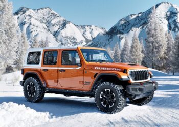 An orange Limited Edition Jeep Wrangler Rubicon is parked on a snowy road, set against snow-covered mountains and trees, celebrating the brand’s 85th Anniversary.