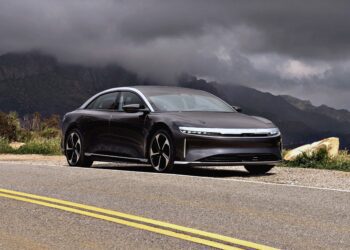 A dark gray luxury sedan, the 2026 Lucid Air Touring, parked roadside with mountains and cloudy skies in the background. Review: 2026 Lucid Air Touring hits the EV sweet spot in both style and performance.