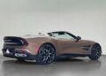A brown Aston Martin Vanquish convertible sports car with black alloy wheels is parked indoors, shown from the rear three-quarter angle.
