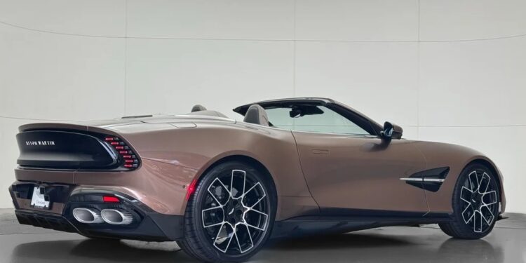 A brown Aston Martin Vanquish convertible sports car with black alloy wheels is parked indoors, shown from the rear three-quarter angle.