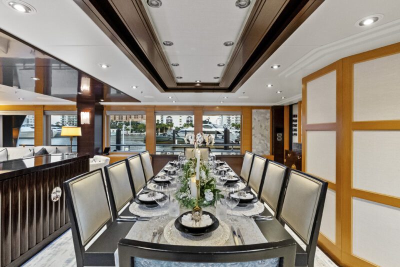 Elegant dining room with a long table set for ten, featuring modern decor, large windows, and an outside view of water and city buildings—offering five-star living aboard the Delta Marine Noverra luxury yacht charter.