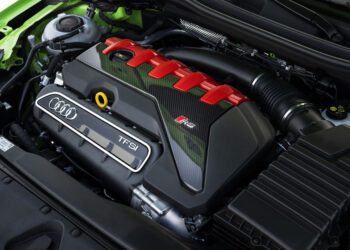 Close-up view of an Audi RS5 engine bay featuring the TFSI engine with red and carbon fiber accents, visible Audi badge, and various components—celebrating the 50th anniversary of the iconic Audi five-cylinder engine.