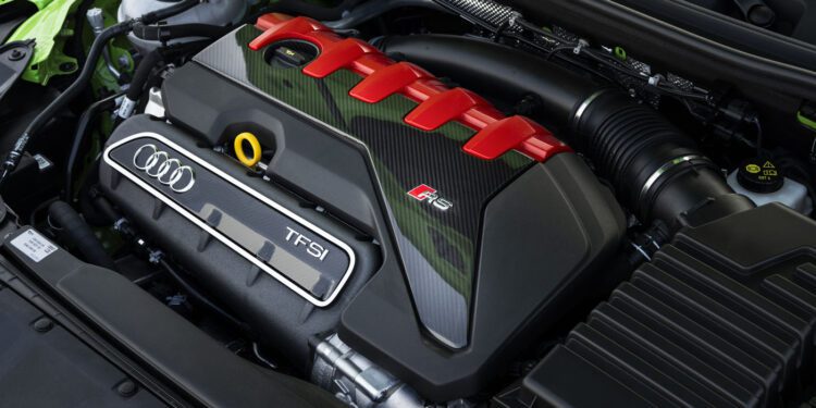 Close-up view of an Audi RS5 engine bay featuring the TFSI engine with red and carbon fiber accents, visible Audi badge, and various components—celebrating the 50th anniversary of the iconic Audi five-cylinder engine.