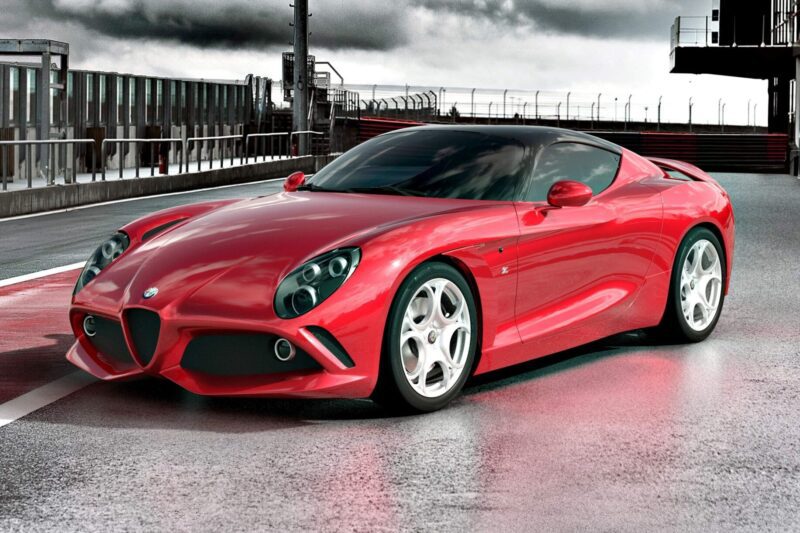 A red sports car parked on a wet race track with metal barriers and a cloudy sky in the background, reminiscent of the thrilling machines from 20 Cars That Focused on Analog engagement in 2025.