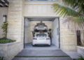 Two cars are parked in a double garage with an Autostacker car lift; a white Tesla sits below while a silver car is elevated above, maximizing garage space.
