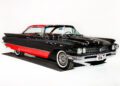 A vintage black and red two-door car with whitewall tires is displayed in a white studio setting, capturing the timeless allure of a Hollywood Classic.